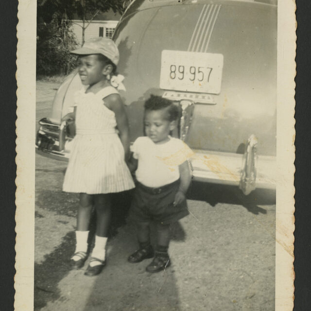 Young Venus Jones and her little brother, Albert, pose for a picture in front of a car.