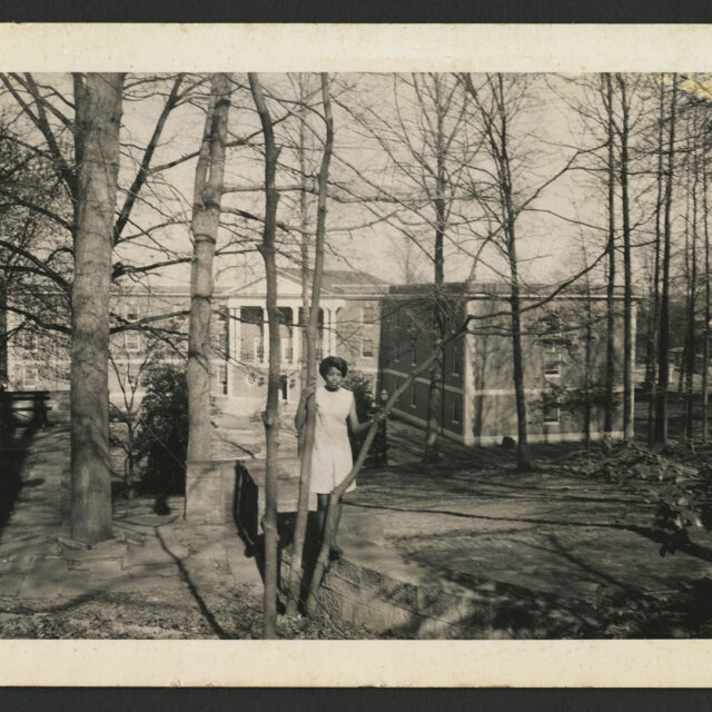 Venus Jones poses for a picture while standing amongst the trees, Mary Washington College's Marshall Hall behind her.