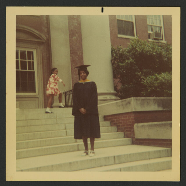 Venus Jones poses for a picture in her cap and gown at her graduation from MWC. She is standing on the steps leading up to a red brick building.