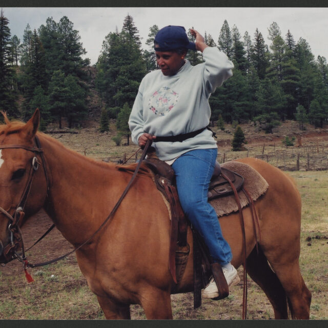 Venus Jones adjusts her baseball cap while riding a chestnut horse in Western tack.