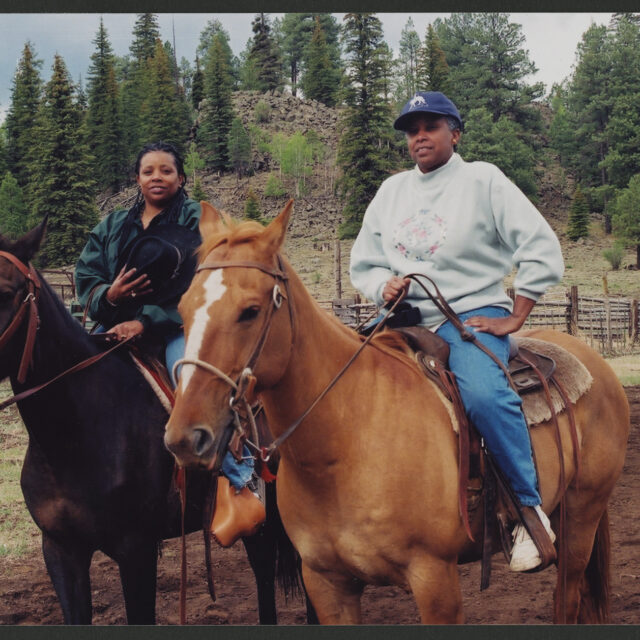 Venus Jones poses for a picture with her sister Vicki. Venus is riding a chestnut horse, and Vicki's horse is a bay. Both are in Western tack.