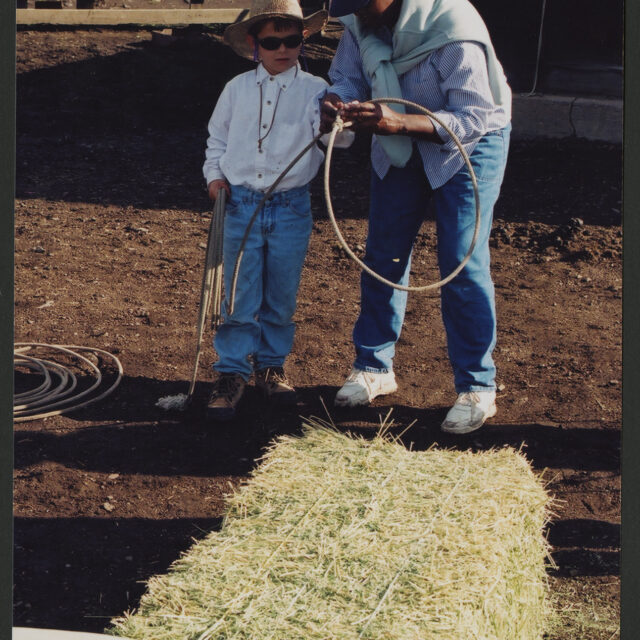 Venus Jones stands behind a hay bale with an imitation cattle's head mounted to it as she teaches a young boy how to hold a lasso.